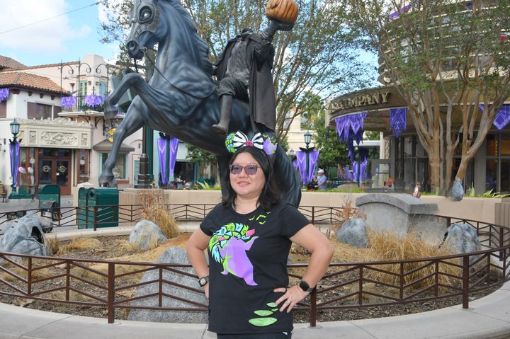 Christine poses in front of headless horseman statue at DCA with Magic Eraser used on background people.