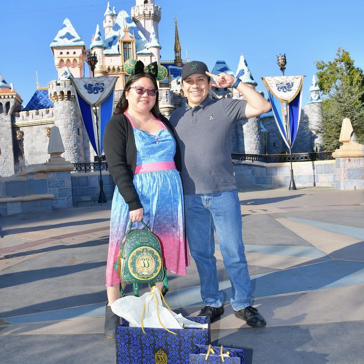 Christine and husband pose in front of Disneyland castle with Club 33 shopping bags with background people removed with Magic Eraser.