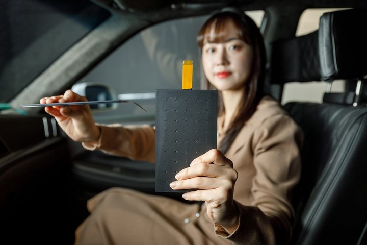 A woman in a car holding the LG Display Thin Actuator Sound Solution speaker.