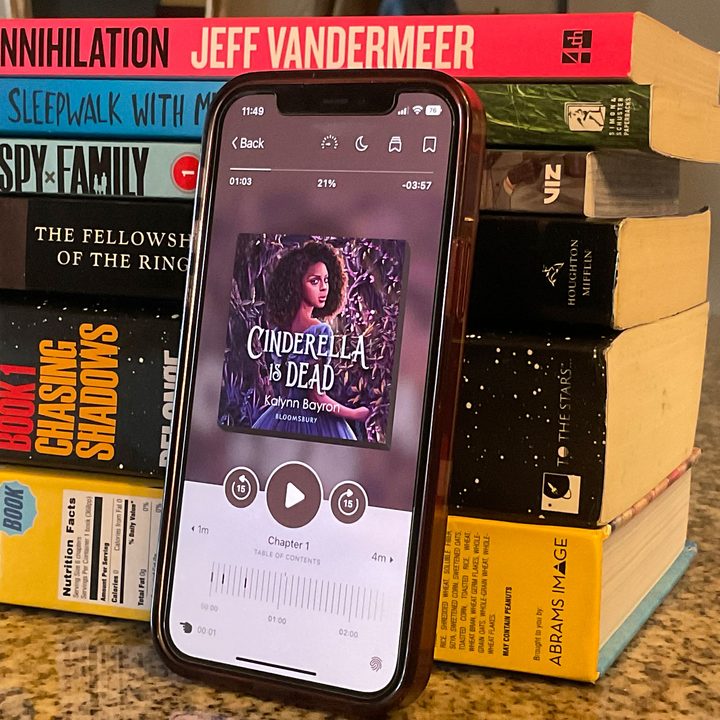 The Libby app displayed on an iPhone 12 leaning on a tower of various books