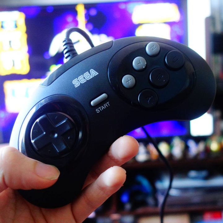 A Sega Genesis Mini controller held up in front of a TV.
