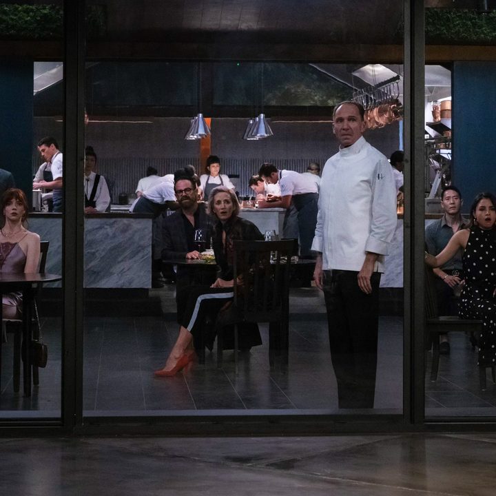 The chef and guests of a restaurant turn and look out the window in a scene from The Menu.