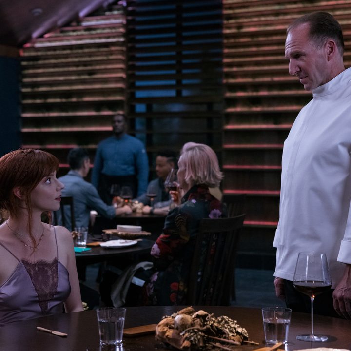 Anya Taylor-Joy sits down and looks up at Ralph Fiennes in a scene from The Menu.