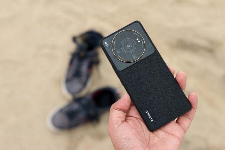 Xiaomi 12S Ultra in gray color against sand and a pair of navy blue shoes.