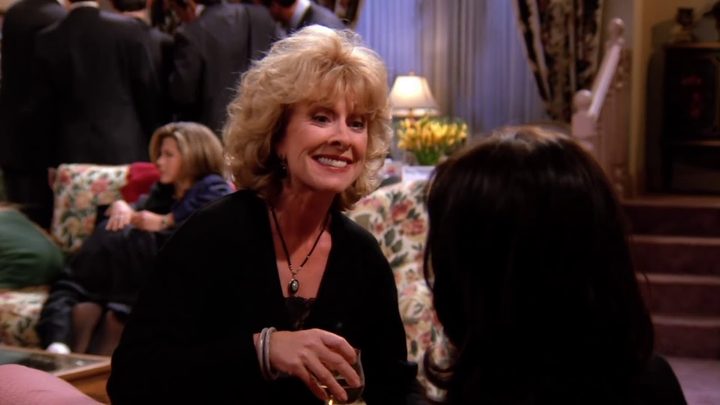 Judy Geller sitting down and smiling at someone in Friends.