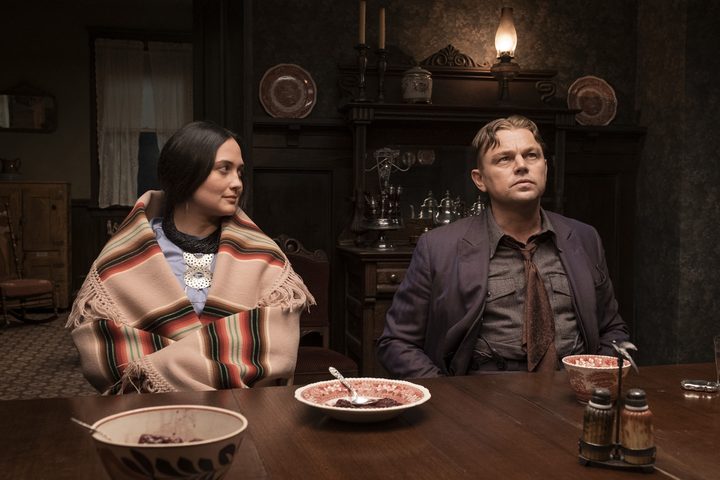 Lily Gladstone and Leonardo DiCaprio sit at a dinner table together in Killers of the Flower Moon.