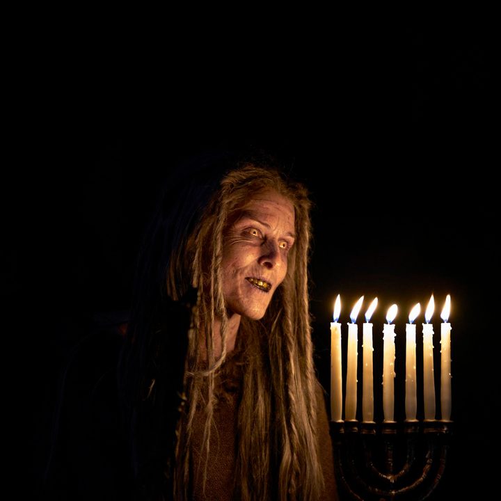 A creature holds a lit menorah n a scene from Lullaby.