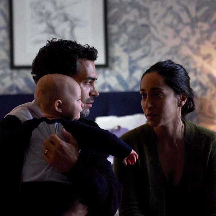 A man holds a baby while his wife looks at him in a scene from Lullaby.