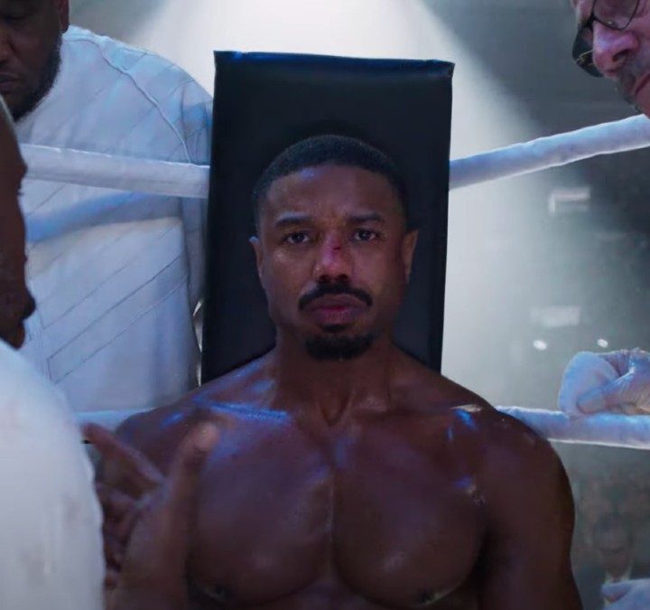 Michael B. Jordan sits on a stool in a boxing ring in Creed III.