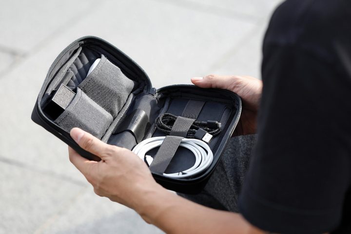 A person holding an open Native Union Stow Organizer, with cables and plugs visible inside.
