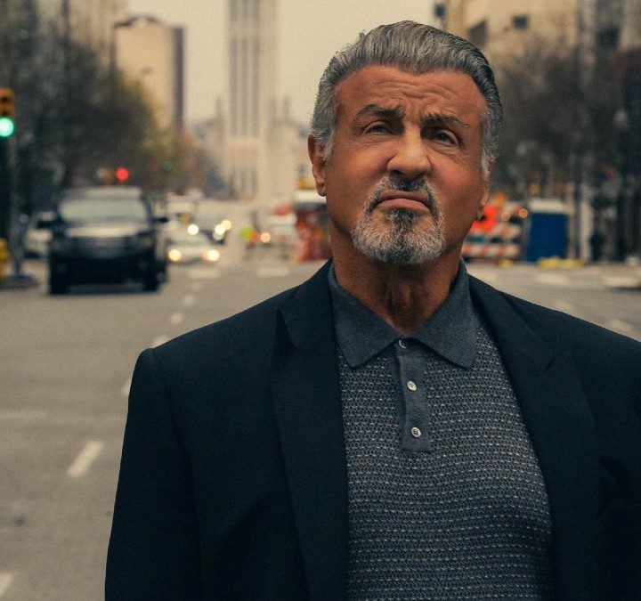 Sylvester Stallone stands in the street and looks up in Tulsa King.