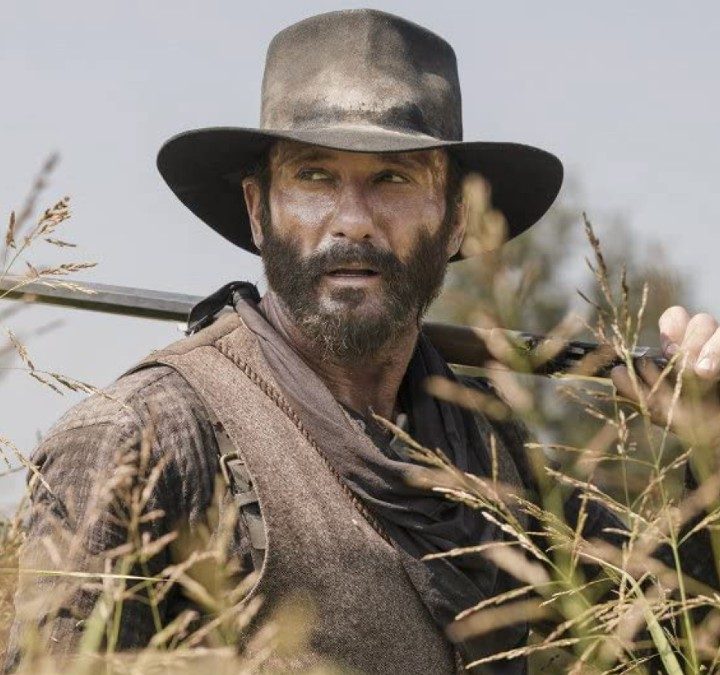 Tim McGraw holds a gun over his shoulder in a scene from 1883.