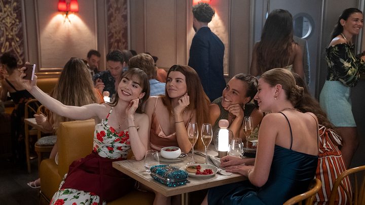 Emily wearing an apron and taking a selfie with restaurant patrons in Emily in Paris.