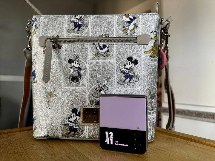 Samsung Galaxy Z Flip 4 Bora Purple standing closed with a Disney100 Dooney & Bourke bag