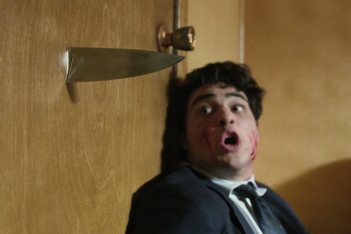 A man looks at a knife puncturing a door in The Recruit.