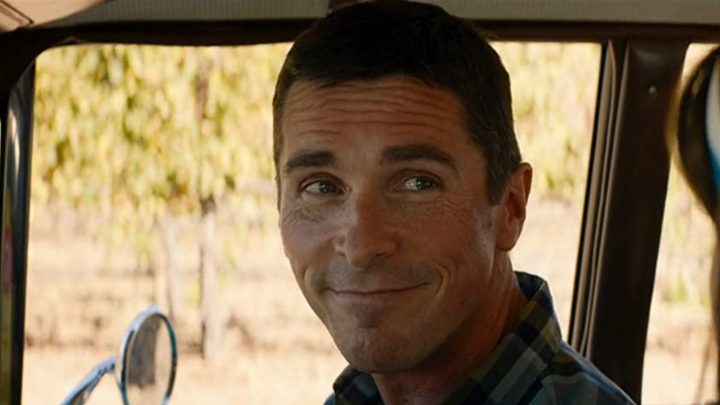 Christian Bale smiles in the front seat of a car in Ford v Ferrari.