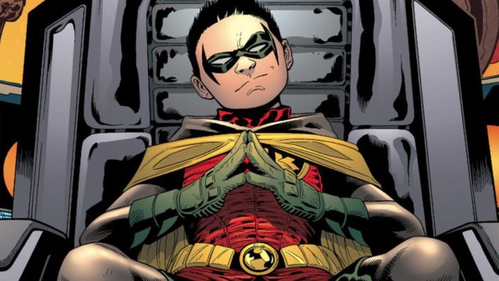 Damian Wayne sitting on a chair and smiling mischievously in DC Comics.