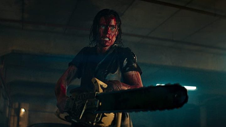 A woman with a bloody face holds a chainsaw in a scene from Evil Dead Rise.