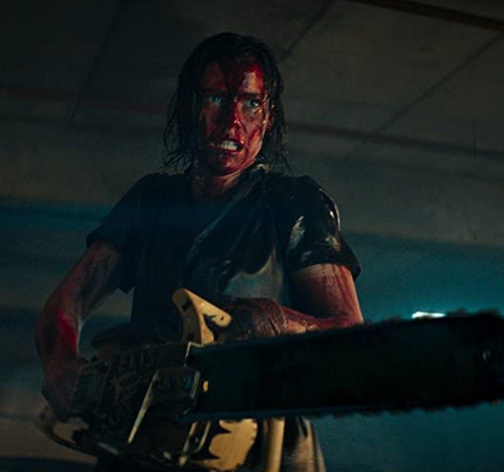 A woman with a bloody face holds a chainsaw in a scene from Evil Dead Rise.