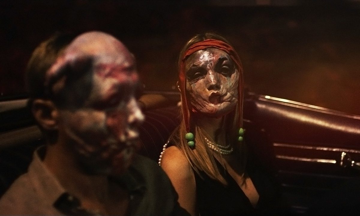 Two people in masks ride in a car in Infinity Pool.