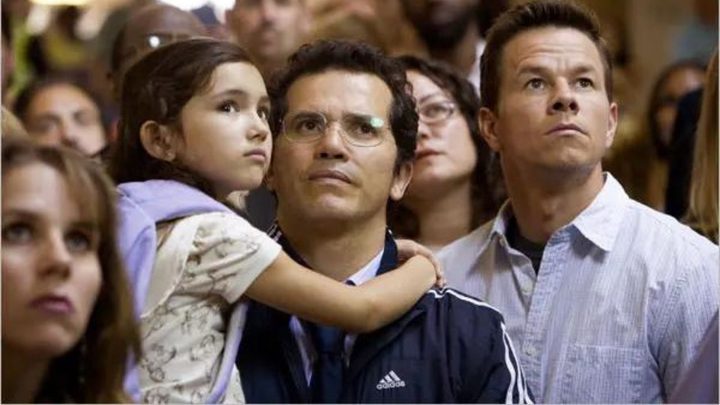 Two men and a crowd paying attention to something off-camera in the movie The Happening.
