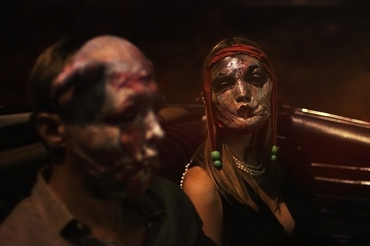 Two masked characters sit in a car together in Infinity Pool.
