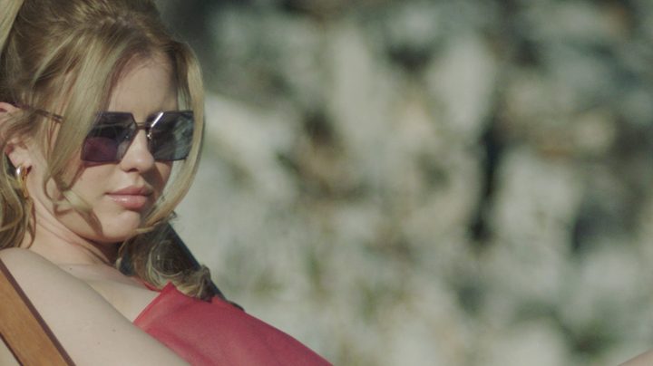 Mia Goth sits on a beach in Infinity Pool.