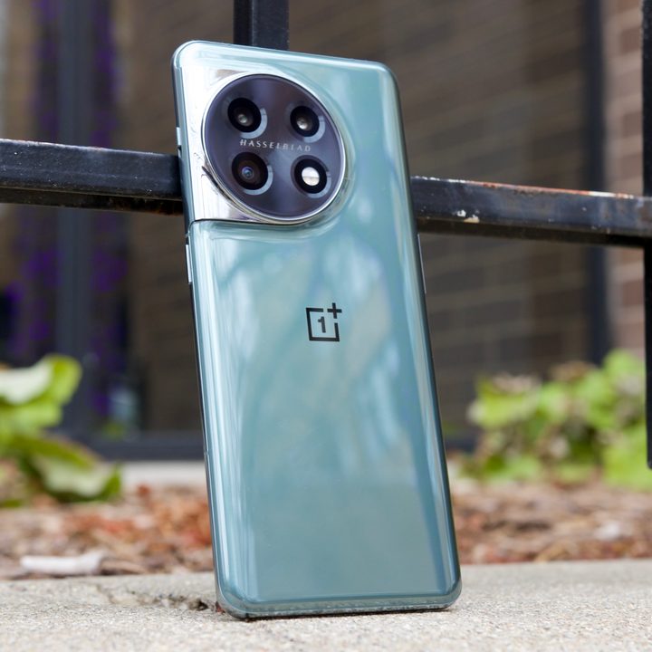 The OnePlus 11, resting upright against a metal rail.