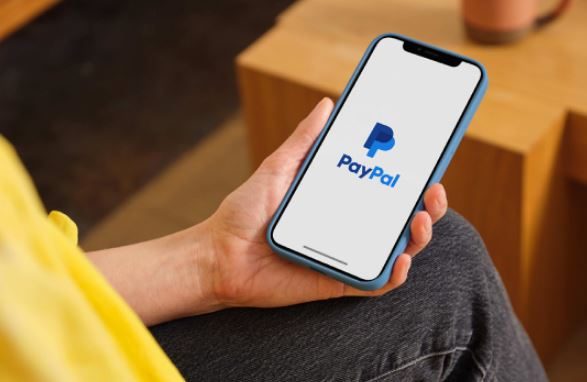 A person holds a mobile phone with the PayPal app open.