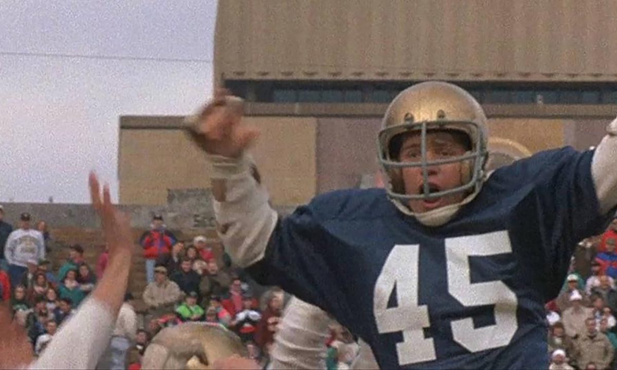Sean Astin in a football uniform being hoisted in the air by others in a scene from the movie Rudy.