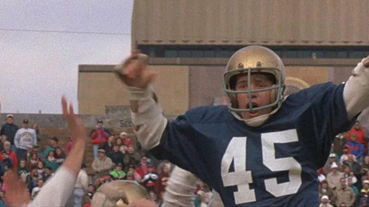 Sean Astin in a football uniform being hoisted in the air by others in a scene from the movie Rudy.
