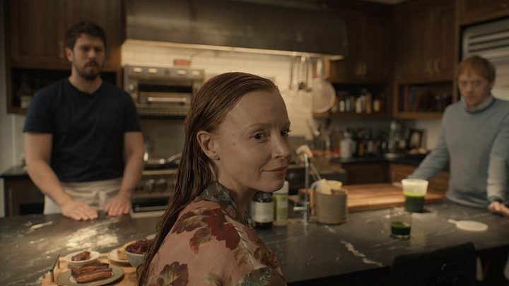 Dorothy looking at something, Sean and Julian in the background in Servant on Apple TV+.