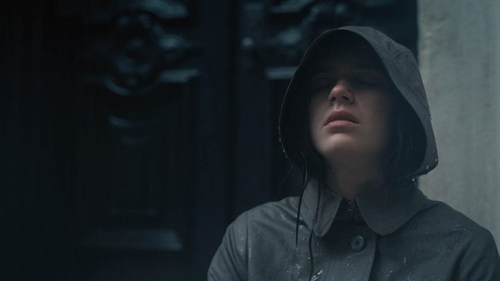 Leanne from Servant wearing a black hooded jacket, eyes closed facing up to the sky.