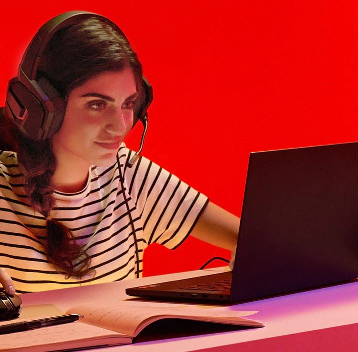 A woman sits by a desk and plays a game on a laptop equipped with an AMD processor.