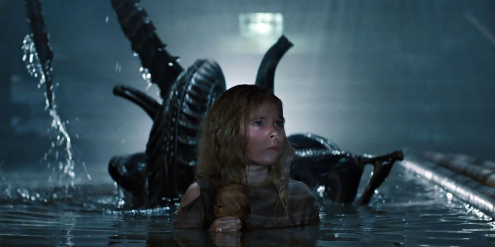 An alien rises up from the water behind Newt in a sewer system.