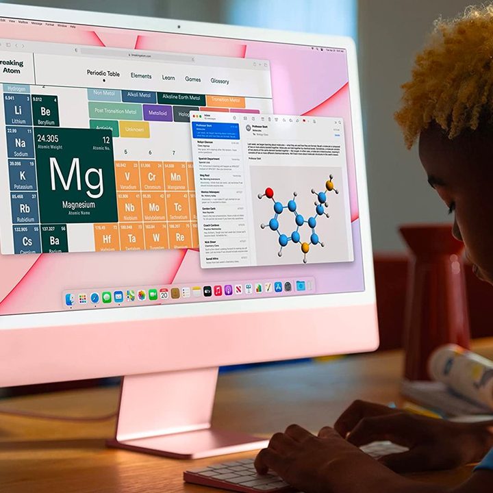 A student types at a desk on a pink Apple iMac 24-inch M1 desktop computer.