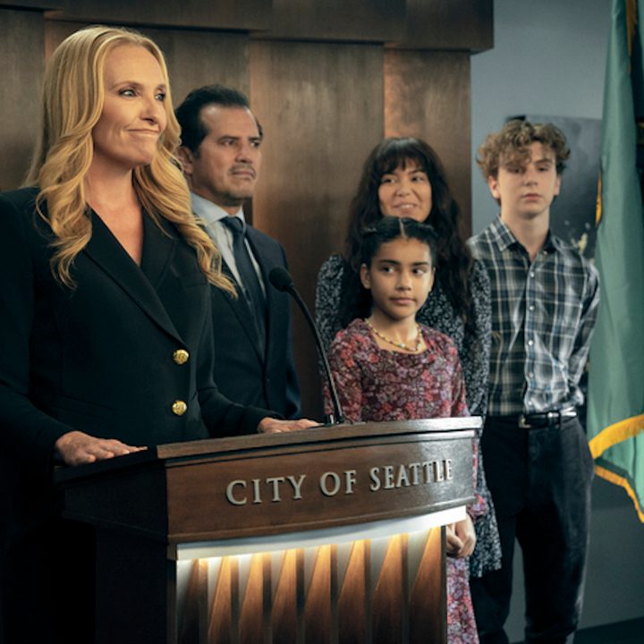 A woman stands at a podium with her family behind her in The Power.