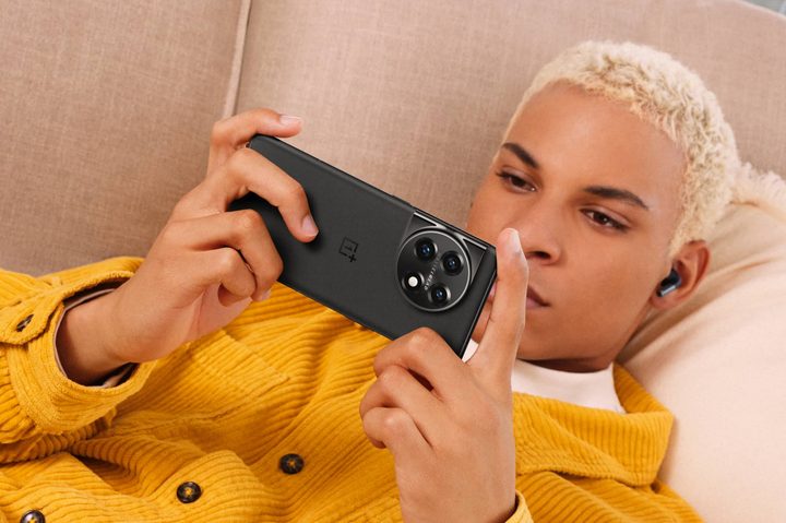 A person laying down while holding a Titan Black OnePlus 11.