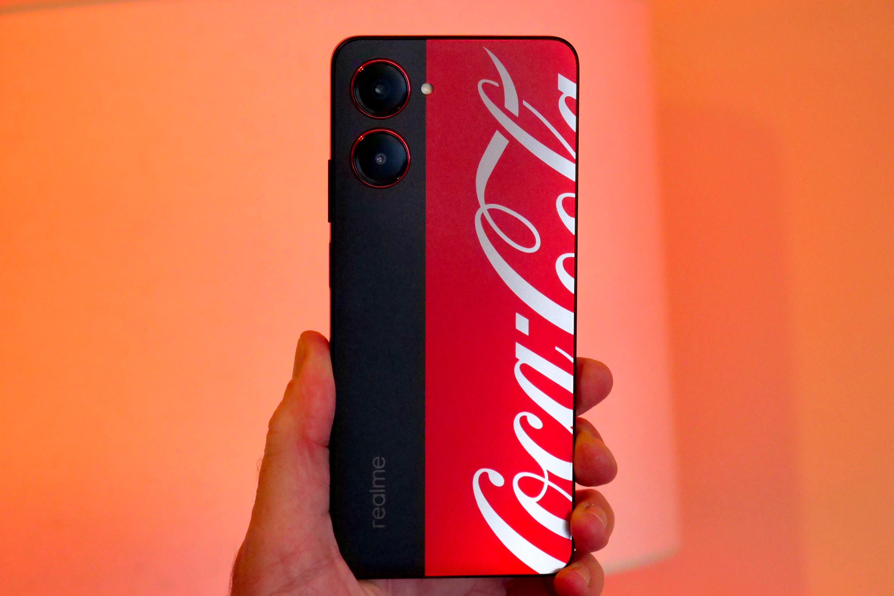 The Realme X Coca-Cola phone held in a person's hand, and seen from the back.