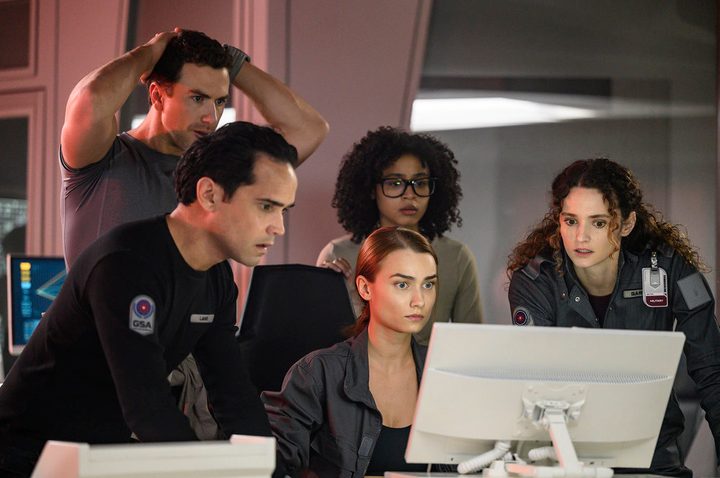 A group of people huddle around a computer in a scene from The Ark.