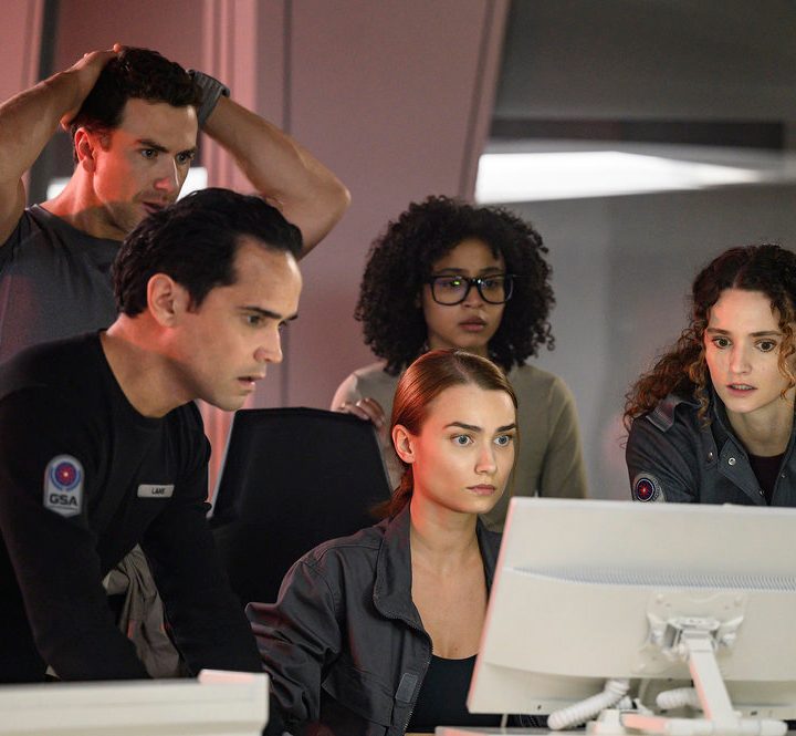 A group of people huddle around a computer in a scene from The Ark.