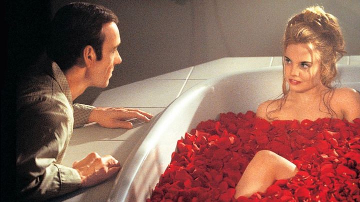 Kevin Spacey crouched by a young girl in a bathtub, covered in rose petals in a scene from American Beauty.