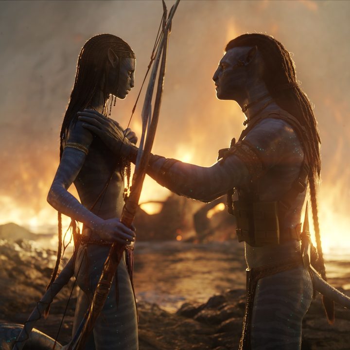 A pair of Na'vi comfort each other in the water while flames spread around them in a scene from Avatar: The Way of Water.