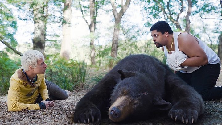 Two men hover over a passed out bear in Cocaine Bear.