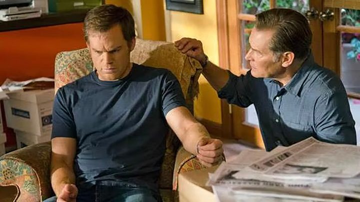 Dexter with his head down, arm on the table looking upset and being comforted by his father in Dexter.