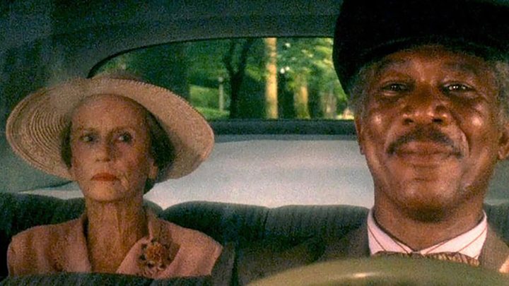 Morgan Freeman smiling while driving Jessica Tandy in a scene from Driving Miss Daisy.