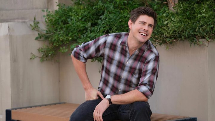 Jesse sitting on a bench, smiling, one hand on his knee in a scene from How I Met Your Father.