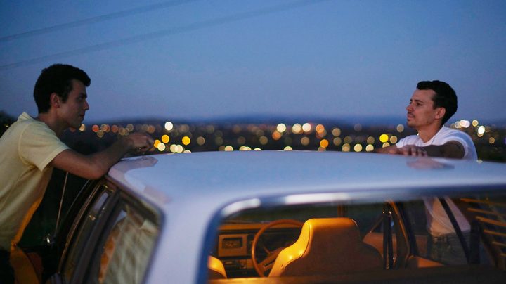 Two men talk to each other at a car in Of an Age.