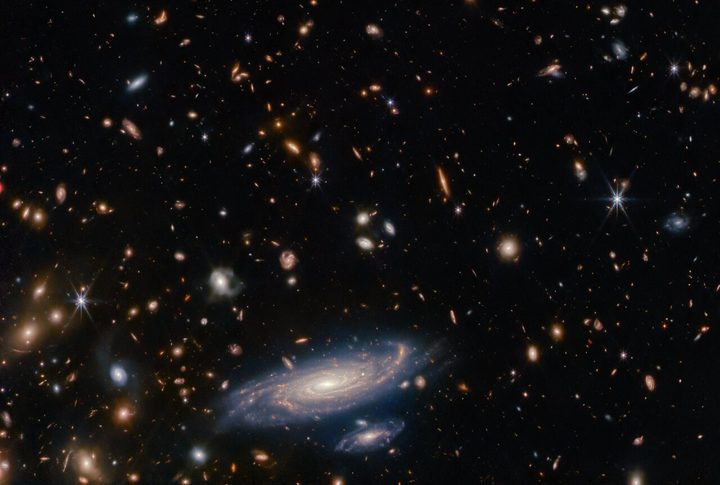 A crowded field of galaxies throngs this Picture of the Month from the NASA/ESA/CSA James Webb Space Telescope, along with bright stars crowned with Webb’s signature six-pointed diffraction spikes. The large spiral galaxy at the base of this image is accompanied by a profusion of smaller, more distant galaxies which range from fully-fledged spirals to mere bright smudges. Named LEDA 2046648, it is situated a little over a billion light-years from Earth, in the constellation Hercules.