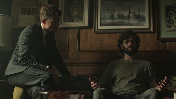 Joe distraught on the couch, Rhys kneeling over him in a scene from You season 4.